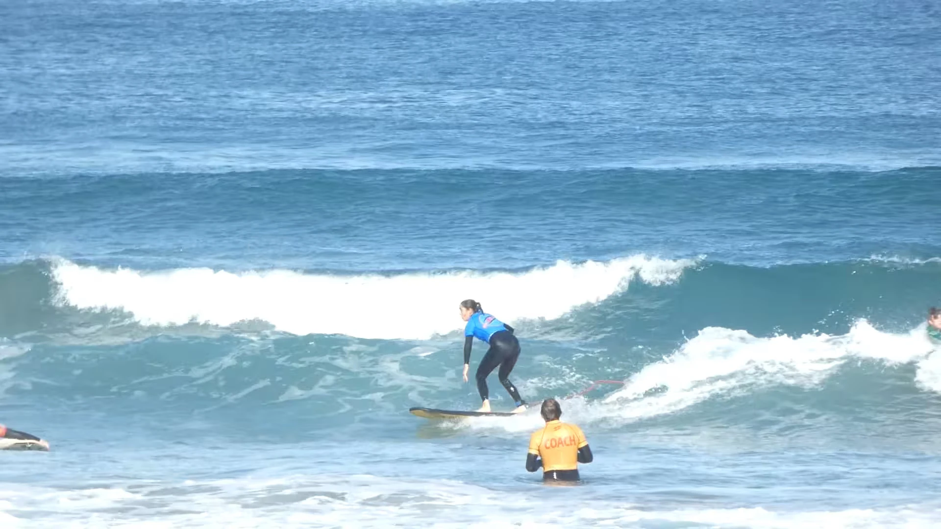 Surfer riding along a green wave, monitored by the coach of the surf school in a session for intermediate and advanced surfers 