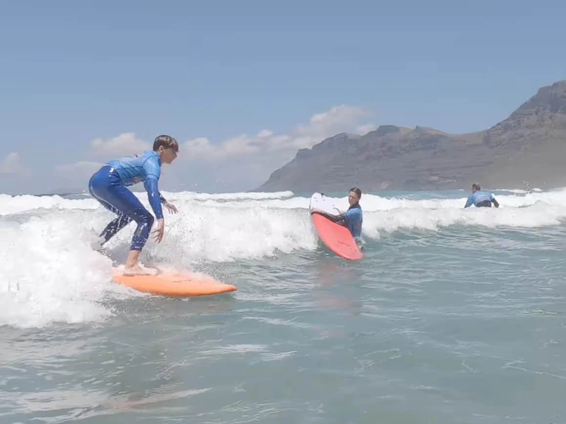 A surfer passes two other participants in a surf course with a surfschool in Famara as he is riding the wave towards the beach