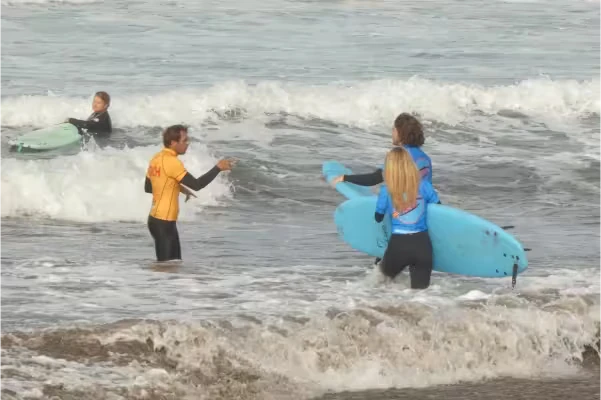 Un instructor privado de surf y dos surfistas entran al agua con sus tablas mientras las olas rompen a su alrededor.