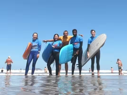 El coach de la escuela de surf Conrad con cuatro alumnos y tablas de surf en el agua poco profunda de Playa de Famara.