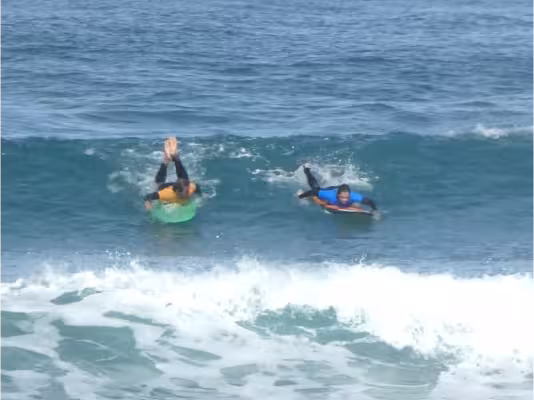 A surfer working paddeling for a green wave, guided by his coach, right before the take off.
