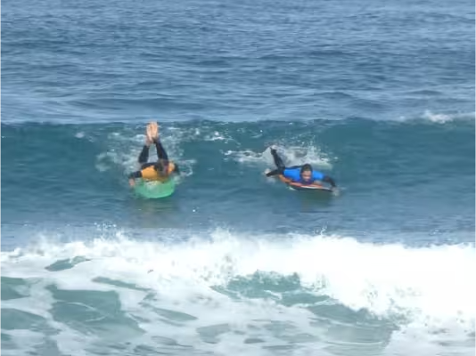 Un surfista rema para coger una ola verde con la guía de su coach, justo antes del take-off.