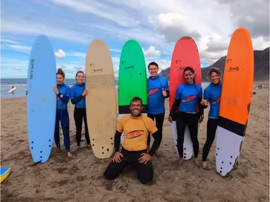 Surf coach Conrad with five students holding colourful surfboards after a lesson at Playa de Famara.