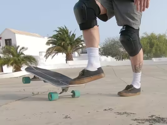 Primer plano de una tabla de surfskate y de los zapatos y las piernas de una persona que gira la tabla con un pie para colocarla en la posición inicial.