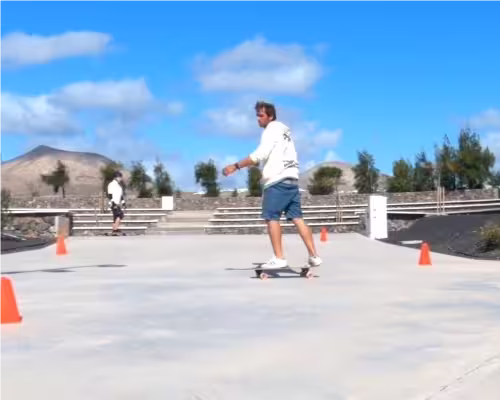 Surf coach Conrad demonstrating tight frontside-to-backside turns around cones while a student practises in the background.