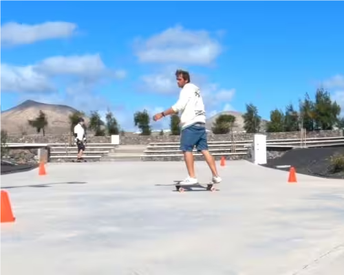Surf coach Conrad demonstrating tight frontside-to-backside turns around cones while a student practises in the background.